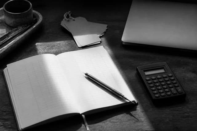 Open business ledger, calculator, laptop, and inventory tags on a desk